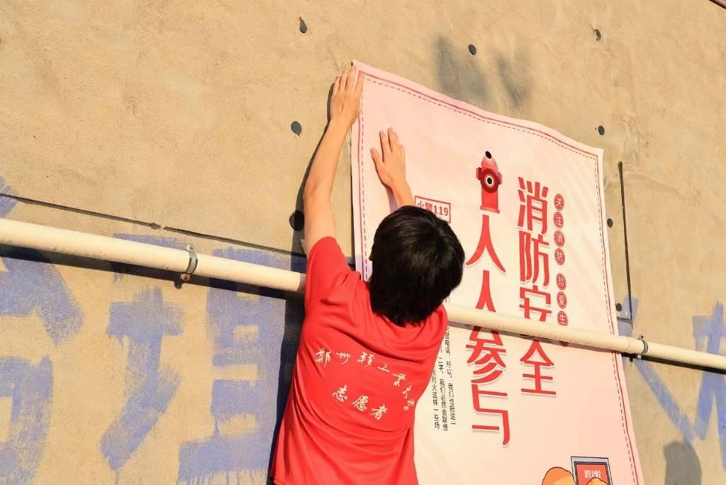 图为团队队员在广场墙壁上张贴消防安全海报。红色的队服、消防安全字样在落日余晖的映衬下交相辉映。中国青年网通讯员 黎泳彤 摄